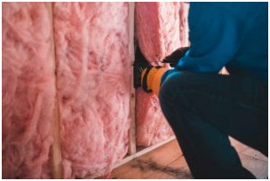 Technician installing pink fiberglass insulation in a wall.